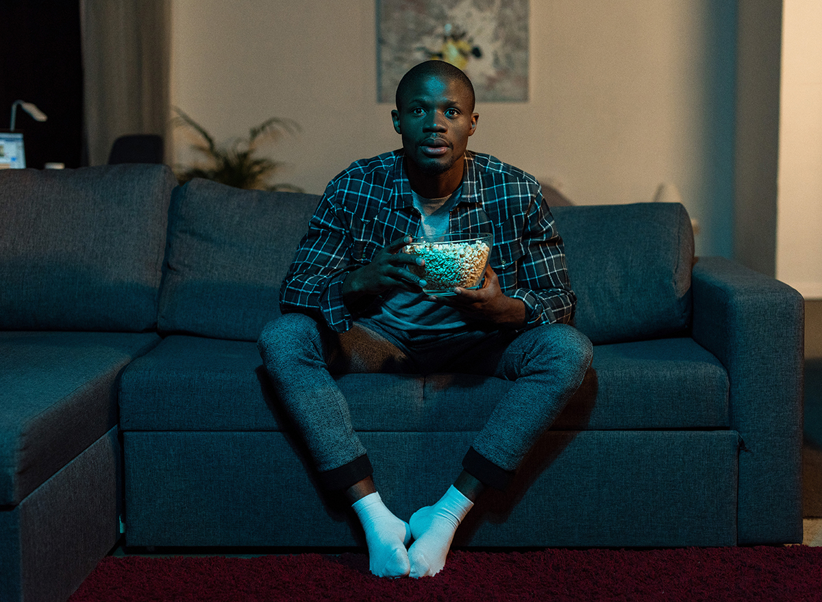 man watching tv on couch holding popcorn bowl