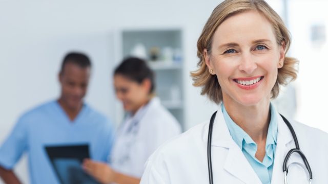 Woman doctor smiling and looking to the camera while a medical team is working.