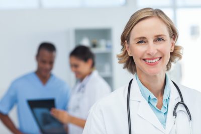 Woman doctor smiling and looking to the camera while a medical team is working.
