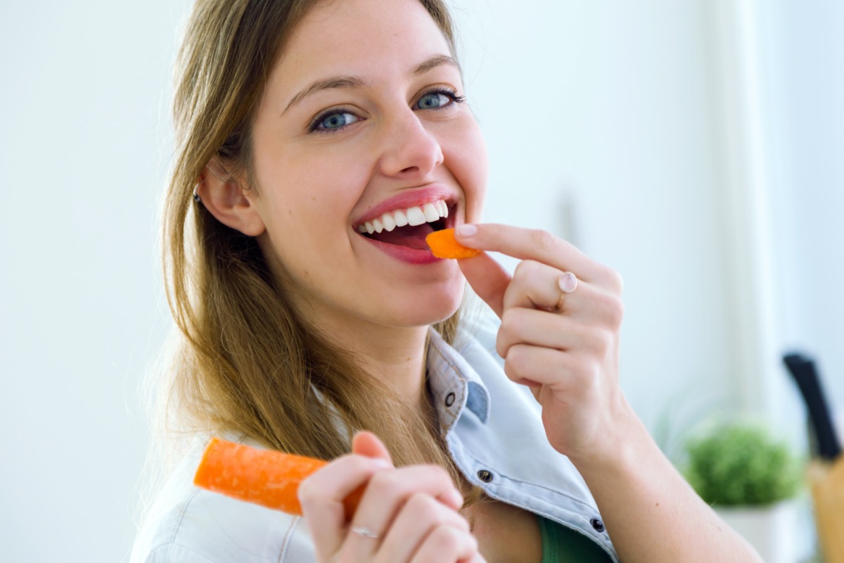 Woman eating carrot in the kitchen.