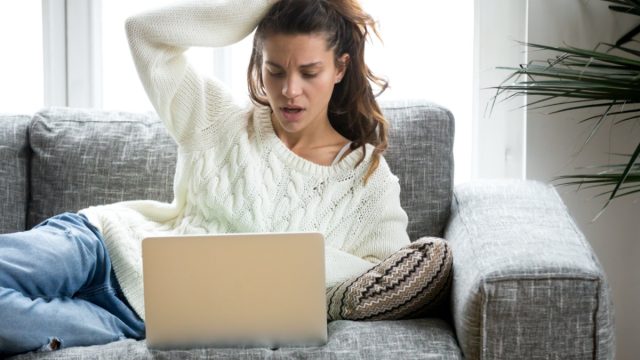 Shocked young woman looking at laptop computer screen at home
