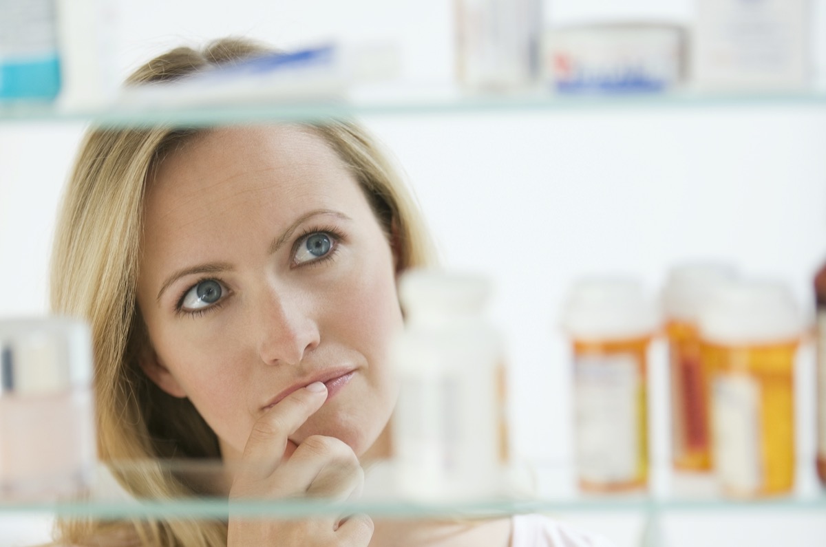 A woman is looking through her medicine cabinet.