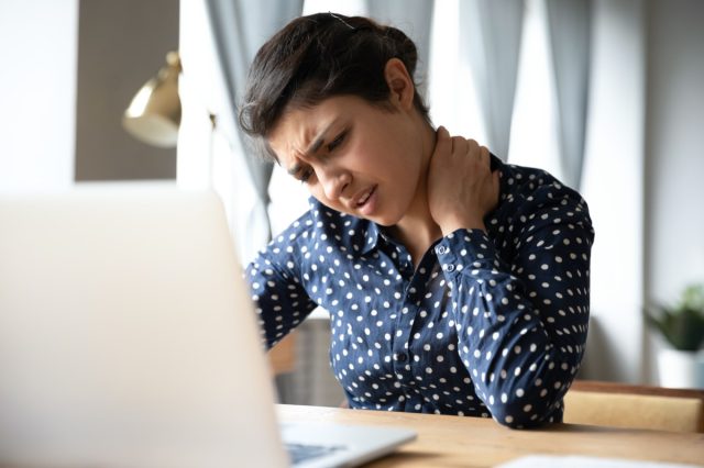 woman sitting at desk in front of laptop, touch neck feels pain.