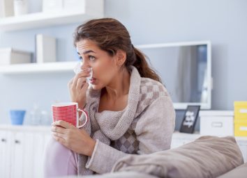 Sick woman blowing nose on her sofa.