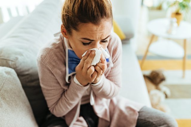 Young woman feeling sick and sneezing in a tissue at home.