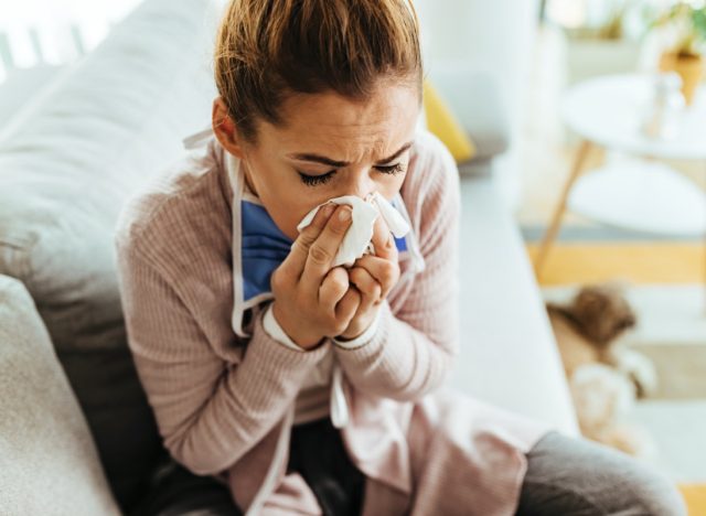 Young woman feeling sick and sneezing in a tissue at home.