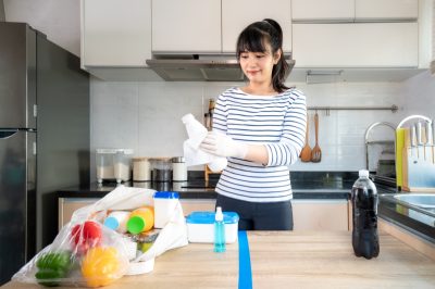 woman laying out groceries on a divided table and wiping down yogurt or milk containers bottle with disinfectant take to eliminate the chances of contamination COVID-19.