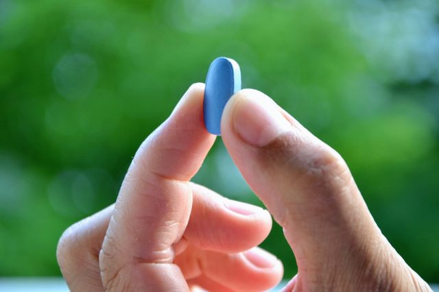 Man's hand holding blue pill.