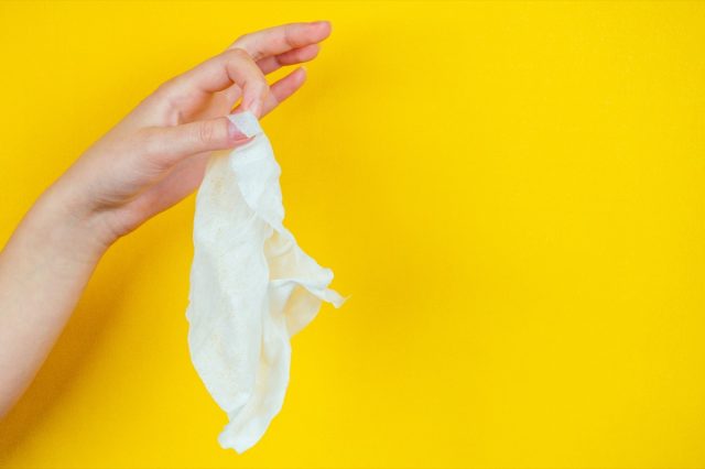 A hand holds a dirty used napkin on a yellow background.