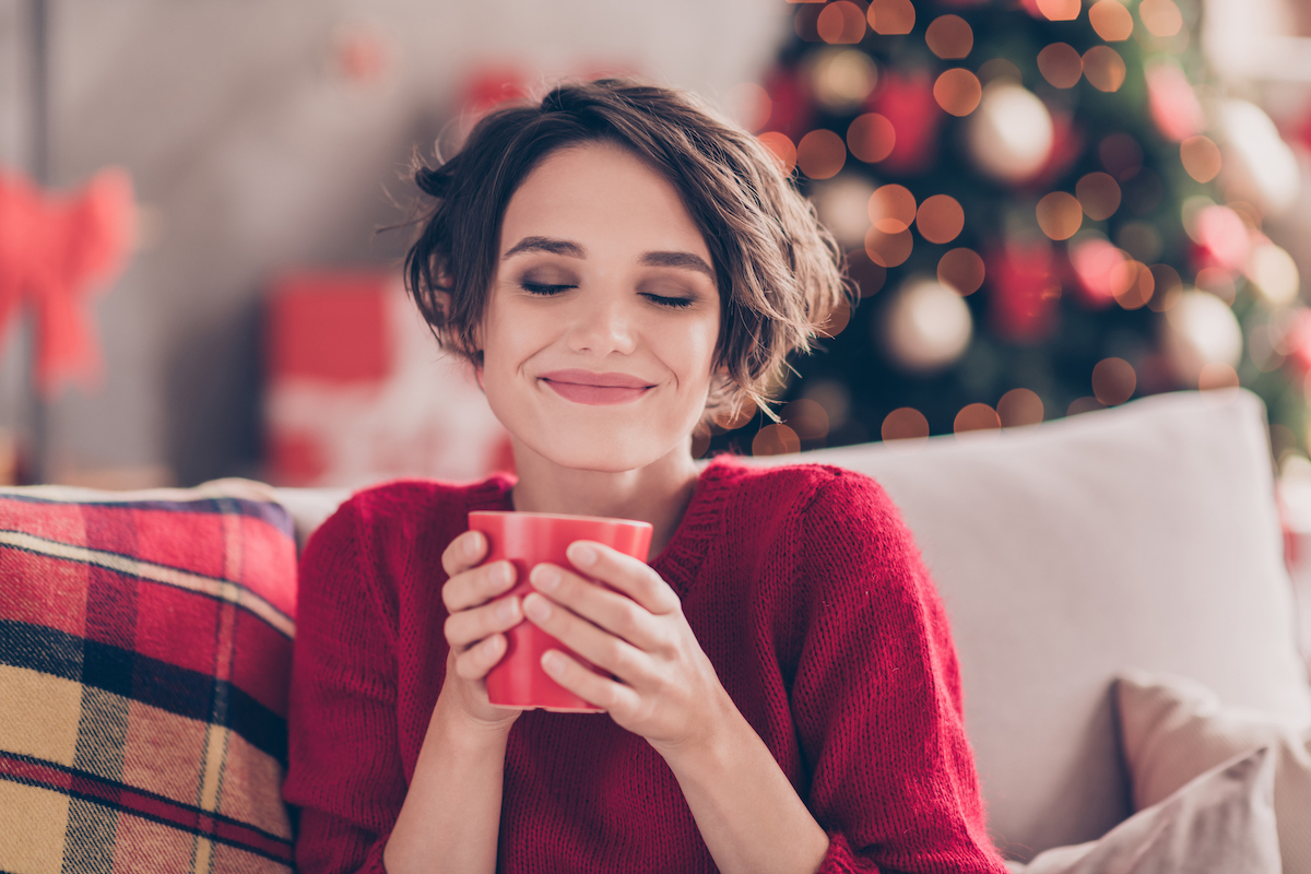 happy woman on couch over christmas drinking tea
