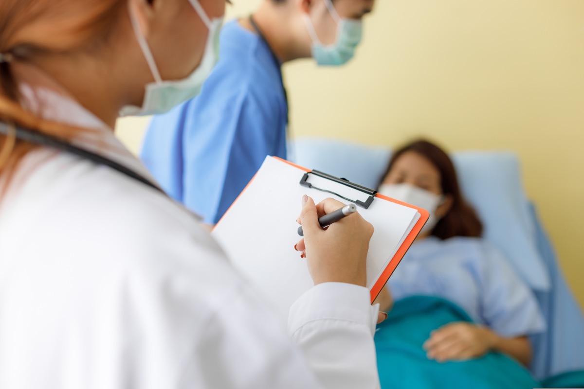 Des médecins féminins et masculins portant des masques et des uniformes visitent pour vérifier les symptômes des patientes d'âge moyen allongées dans leur lit.