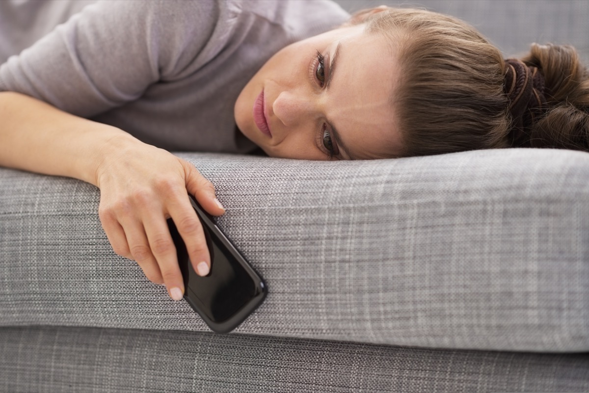 A woman lying on a sofa holding a phone.