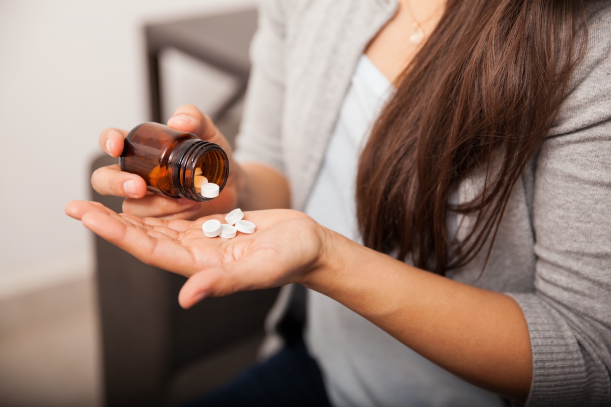 Closeup of a young brunette getting some aspirins from a bottle at home.