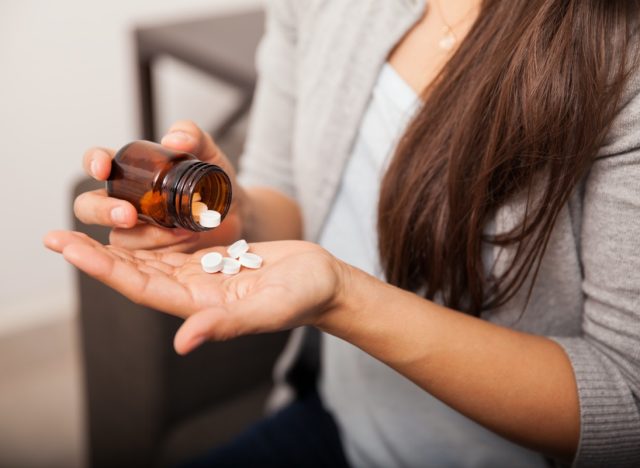Closeup of a young brunette getting some aspirins from a bottle at home.