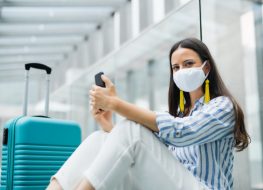 woman with smartphone going on holiday, wearing face masks at the airport