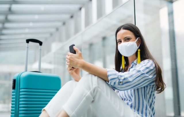 woman with smartphone going on vacation, wearing face masks at airport
