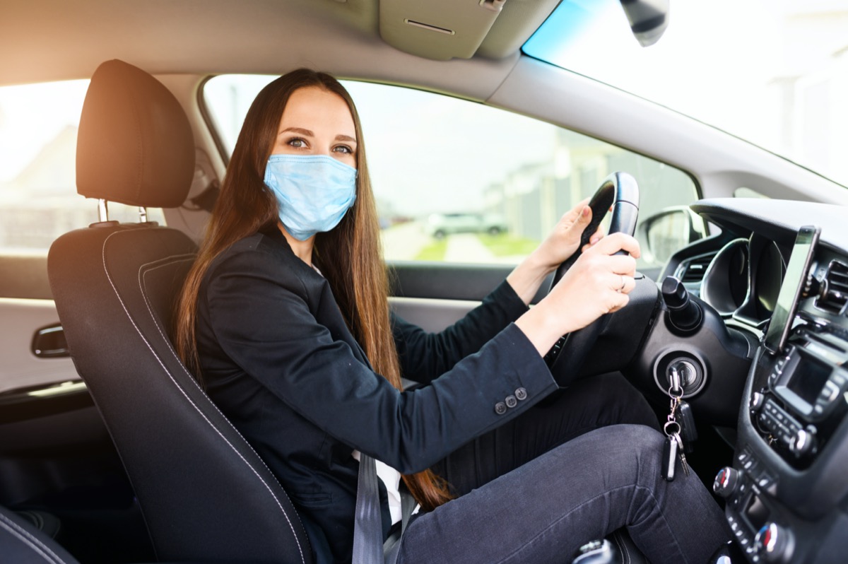 woman with surgery protective mask on her face is driving car.