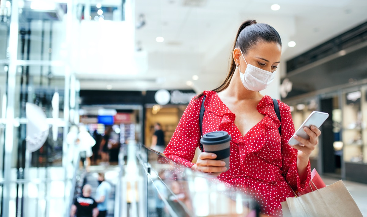 woman wearing a face mask checking her phone in a shopping mall.