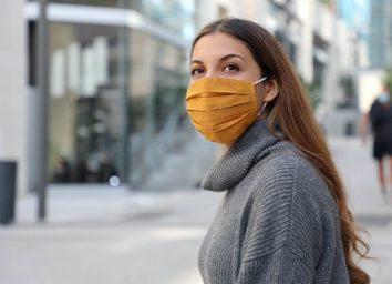 Woman with protective mask looks around on a street.