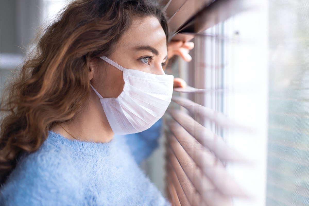 woman wearing a face mask and peeking out from blinds