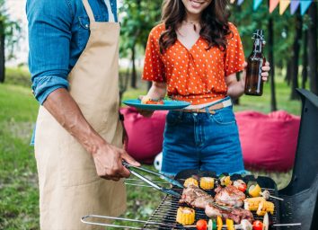 woman with beer looking at african american boyfriend cooking food on grill during barbecue