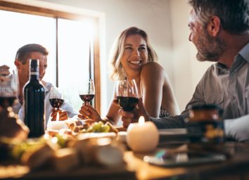 Smiling woman talking with friends sitting at dining tablet at home. Group of people having great time at dinner party.