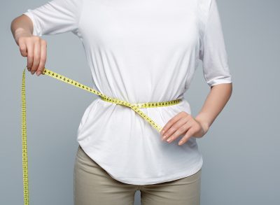 woman in white shirt measuring waist with tape