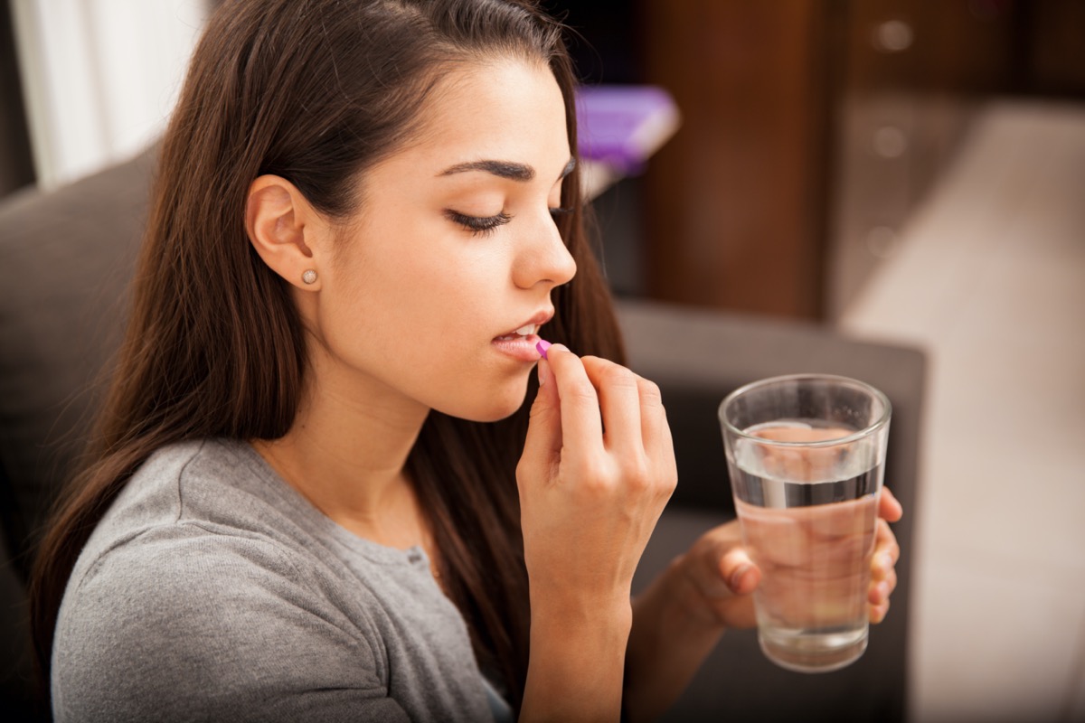 brunette taking a pill with a glass of water at home.