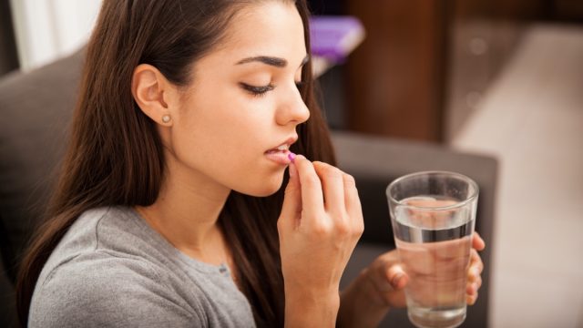 brunette taking a pill with a glass of water at home.