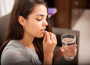 brunette taking a pill with a glass of water at home.