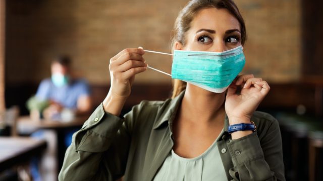Woman putting on face mask while sitting in a cafe during coronavirus.