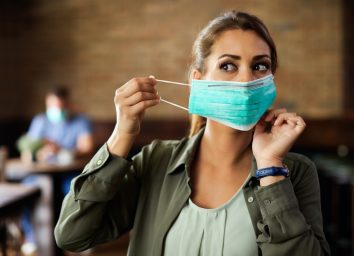 Woman putting on face mask while sitting in a cafe during coronavirus.