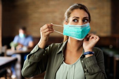 Woman putting on face mask while sitting in a cafe during coronavirus.