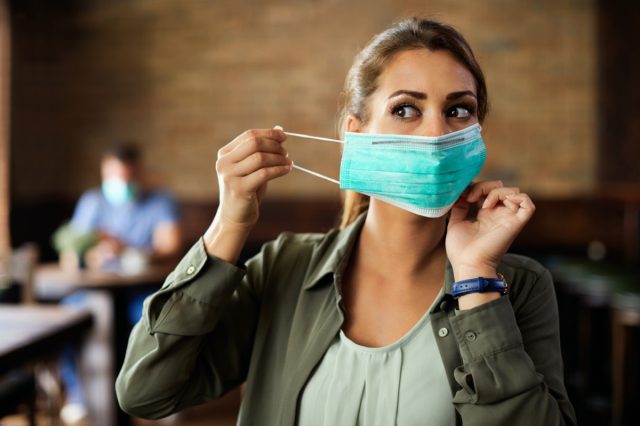 Woman putting on face mask while sitting in a cafe during coronavirus.