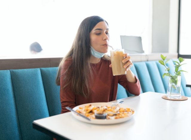 Hispanic young woman having drink in cafe during coronavirus outbreak