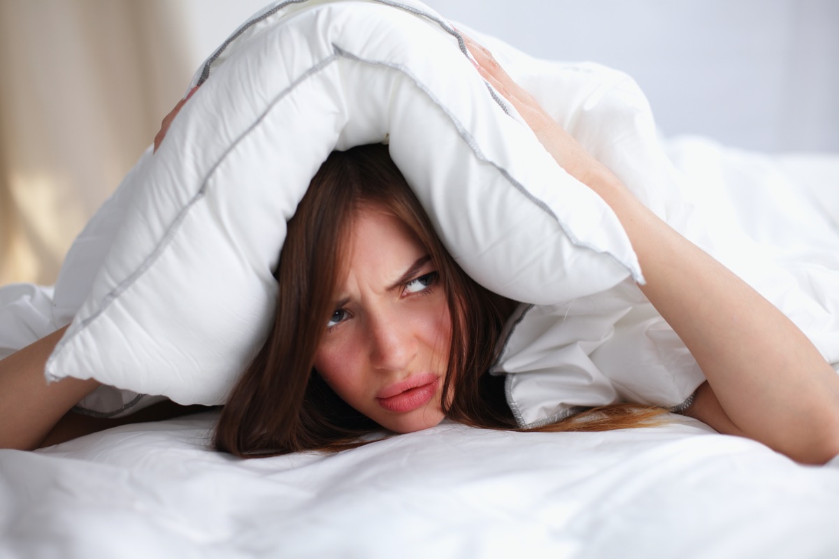 Female lying on bed and closing her ears with pillow