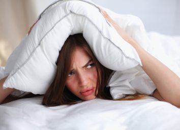 Female lying on bed and closing her ears with pillow