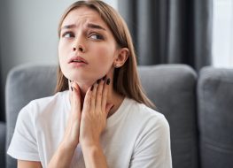 woman touching her neck and feeling pain in throat while sitting in the living room at home.