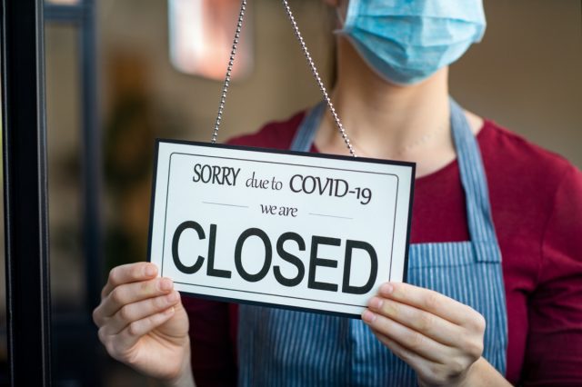Businesswoman closing her business activity due to covid-19 lockdown.  Owner with surgical mask closes his store due to quarantine coronavirus damage.  Big bankrupt business sign due to the effect of the COVID-19 pandemic.