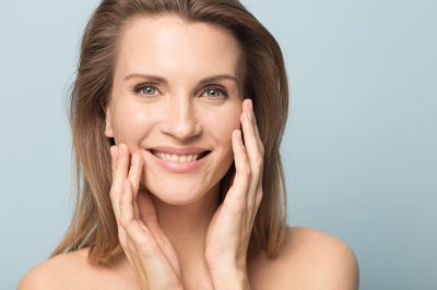 smiling woman touching perfect smooth face skin, looking at camera