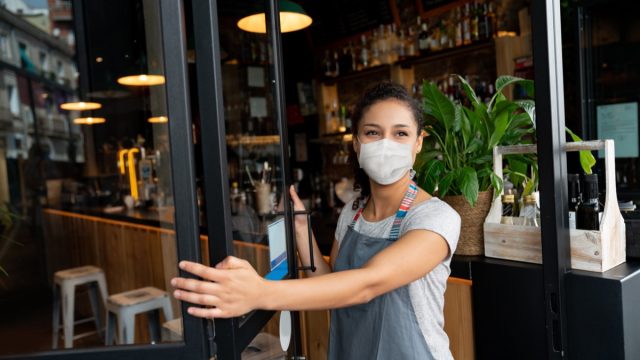 Happy business owner opening the door at a cafe wearing a facemask