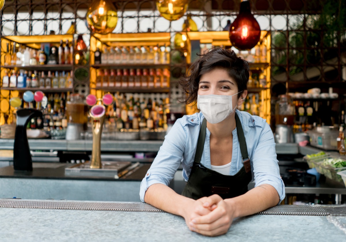 Portrait of a happy waitress working at a restaurant wearing a facemask.