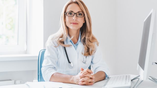 Portrait of adult female doctor sitting at desk in office clinic