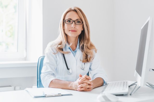 Porträt einer erwachsenen Ärztin, die am Schreibtisch in einer Büroklinik sitzt