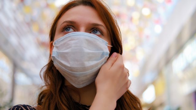 A young woman is considering whether to remove the medical mask after the end of the quarantine due to the coronavirus.