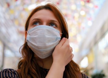 A young woman is considering whether to remove the medical mask after the end of the quarantine due to the coronavirus.