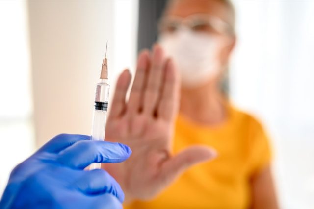 unrecognizable doctor trying to vaccinate its patient while she is refusing it.