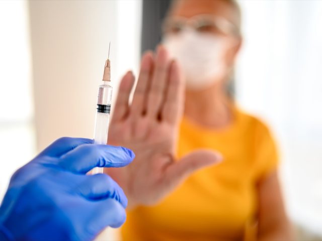 unrecognizable doctor trying to vaccinate its patient while she is refusing it.