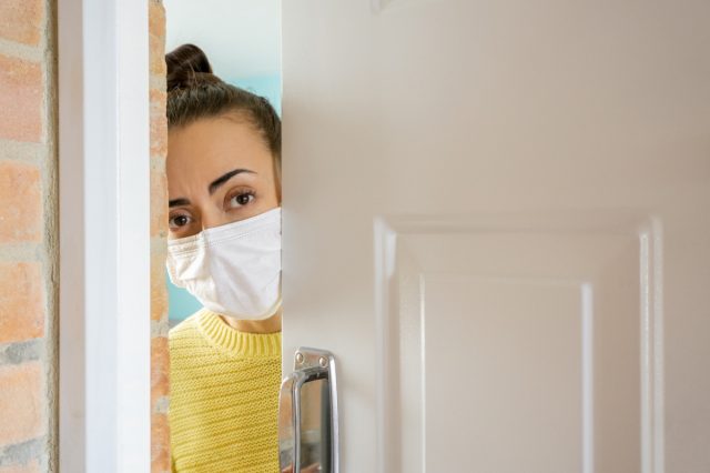 Woman at home opening the door wearing a facemask to avoid the coronavirus.