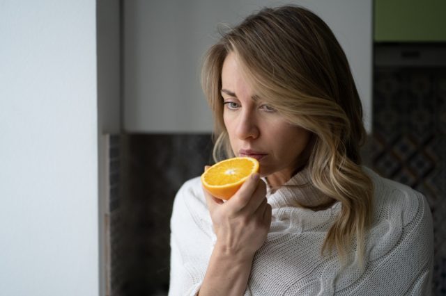 une femme essayant de sentir l'odeur de la moitié d'une orange fraîche, présente des symptômes de Covid-19